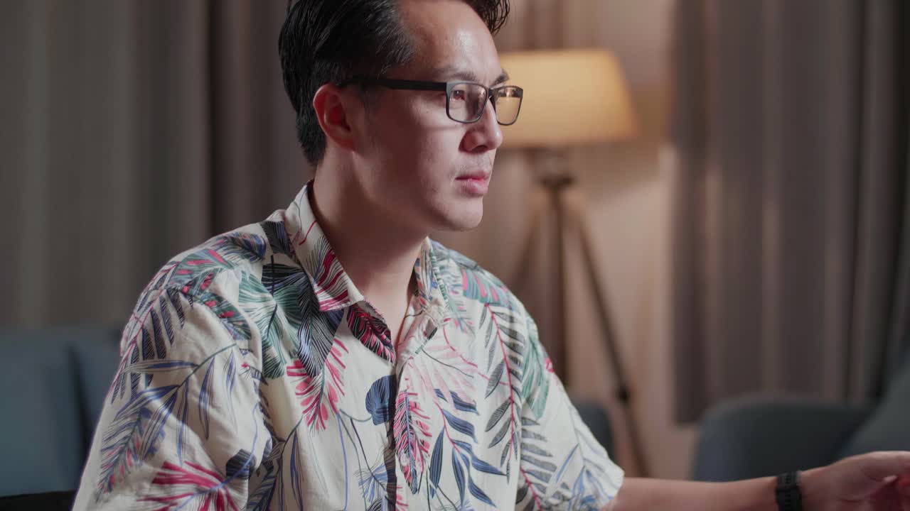 체어에 앉아 있는 아시아인 남자가 집에서 카메라 에 있는 데스크에서 비디오를 편집하는 동안 커피를 마시고 있다.
