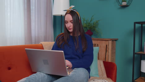 cheerful young woman sitting on sofa, using laptop pc share messages on social media application
