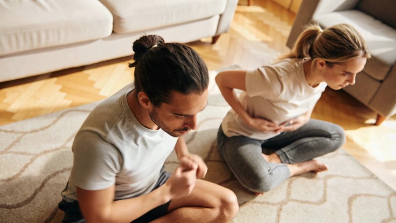 Starting with hands back, couple in grey, white tees rotating torsos on rug for home mobility