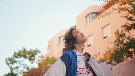 dancing woman listening song in earphones at summer street closeup. girl walking
