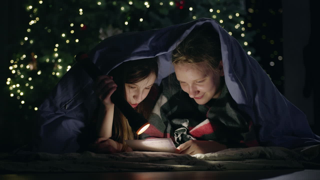 Children Reading Under Blanket by Christmas Tree