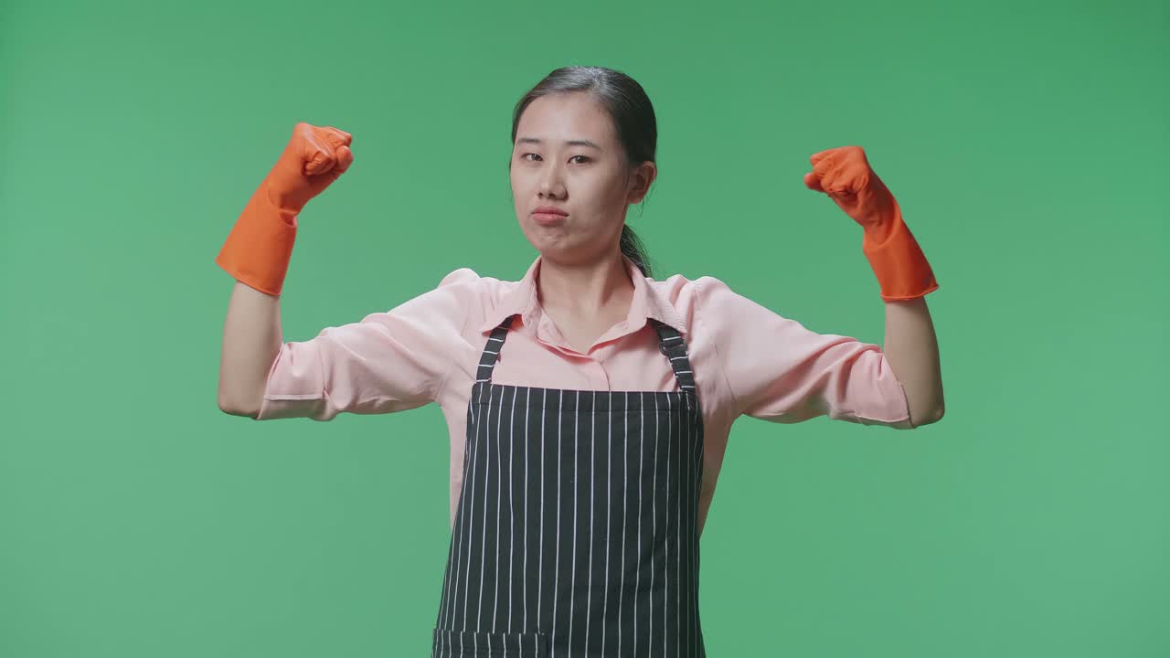 녹색 스크린 스튜디오 에 서 있는 동안 그녀의 비셉스 를 보여주는 아프론 을 입은 아시아 여성 집주인
