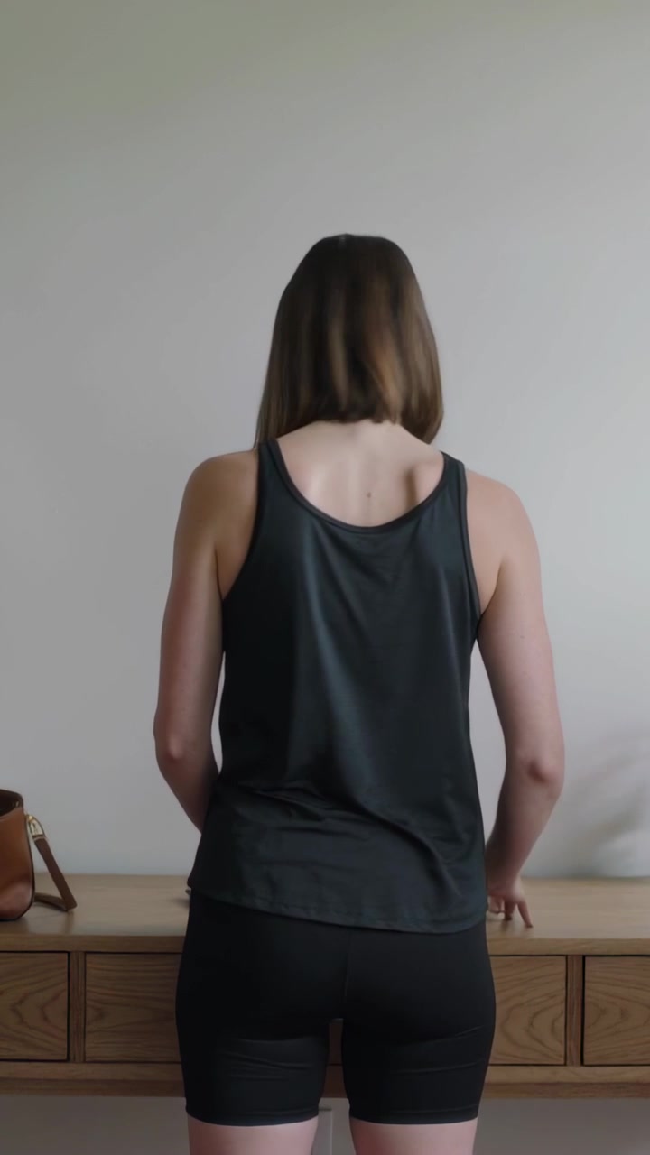 Video verticale: Donna che si allunga per sistemare chiavi e telefono su una consolle nell'ingresso, mentre un braccio entra nell'inquadratura, vestita di nero