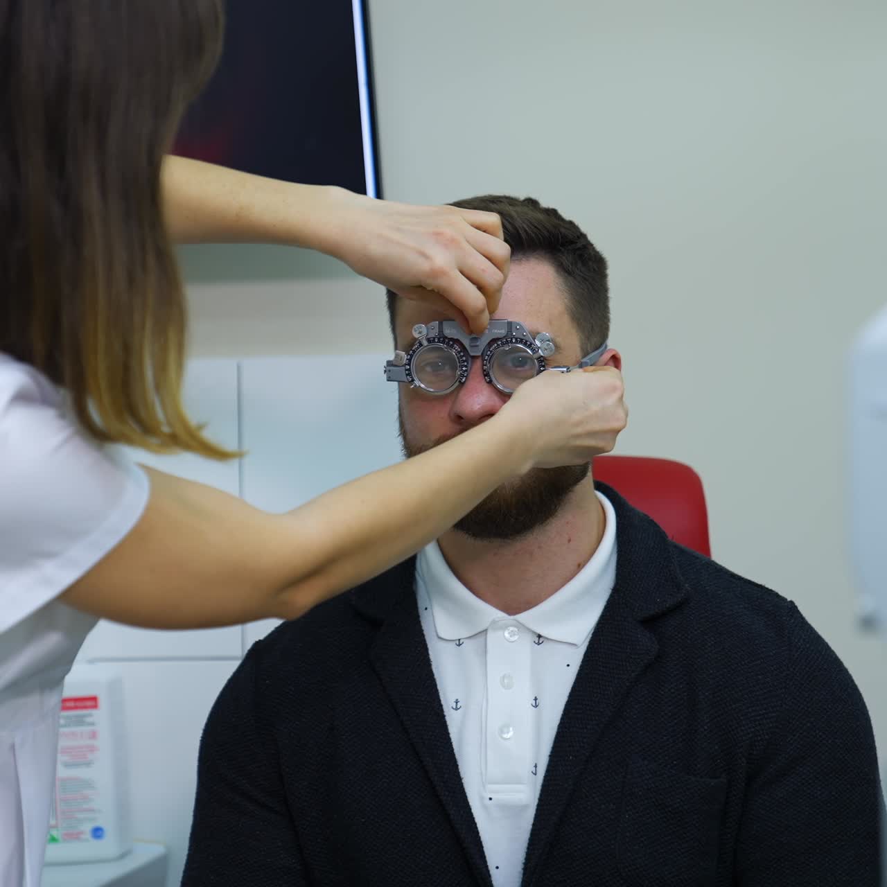 Man examining his eyesight in modern clinic. Doctor ophhalmologist putting on trial frame with lenses on a patient eyes. Slow motion