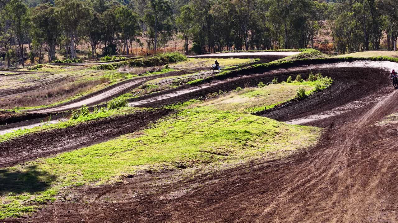 Motocross rider speeds around dirt track curve in daylight, wide shot, natural outdoor setting