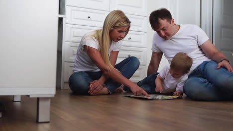 a family of three in white t-shirts and blue jeans sitting on the floor of their bedroom playing with the boy in intellectual games. slow-motion shooting happy family