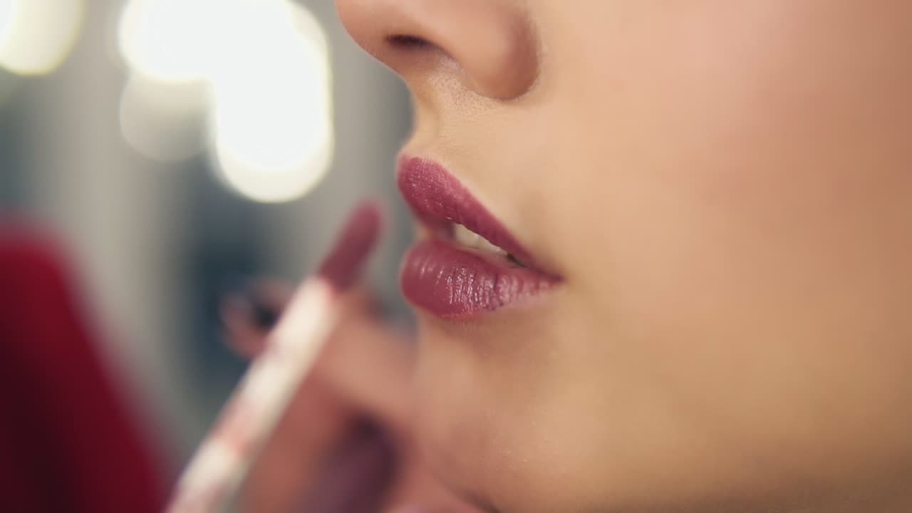 Close Up view of a professional makeup artist applying lipstick on model's lips working in beauty fashion industry. Close Up view