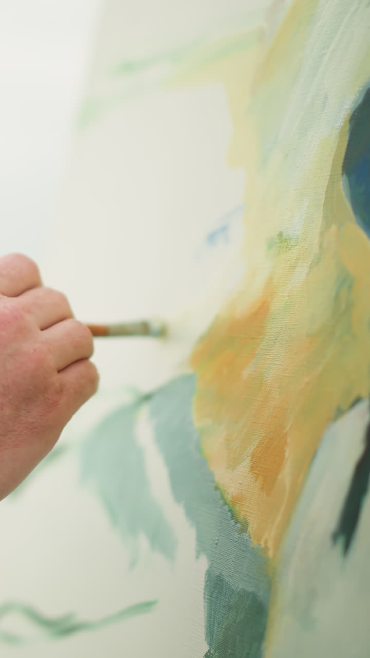 A close-up shot of an artist s hand in a checkered shirt holding a brush as he skillfully and gently paints a vibrant portrait on a canvas