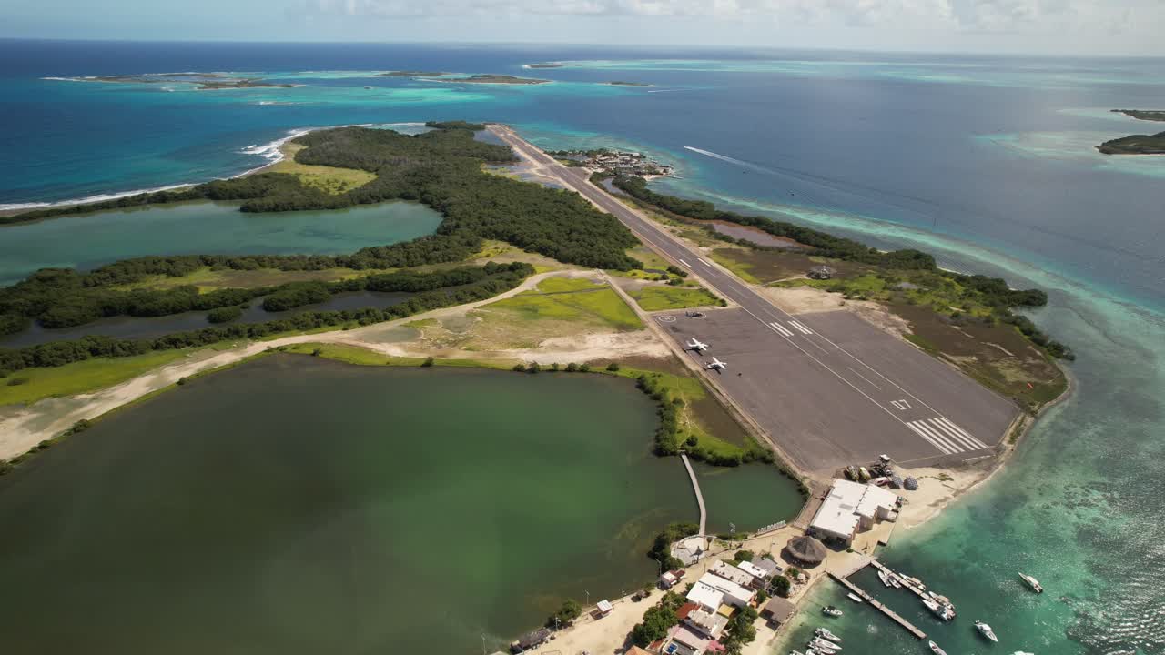 A tropical island airport runway with ocean and greenery, sunny day, aerial view