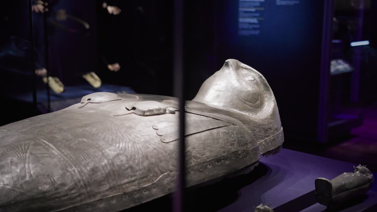Antico sarcofago egizio con geroglifici incisi esposto in una mostra museale scarsamente illuminata, che mette in mostra l'artigianato dettagliato e l'arte funeraria.