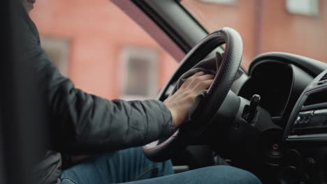 lower view of young adult seated in car wiping leather steering wheel with handkerchief in smooth circular motion through open window highlighting careful hands focus interior details closeup vehicle