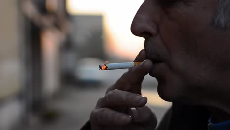 a reflective moment captured: a close-up of a man smoking a cigarette, bathed in warm light, signifying contemplation and relaxation amidst an urban setting