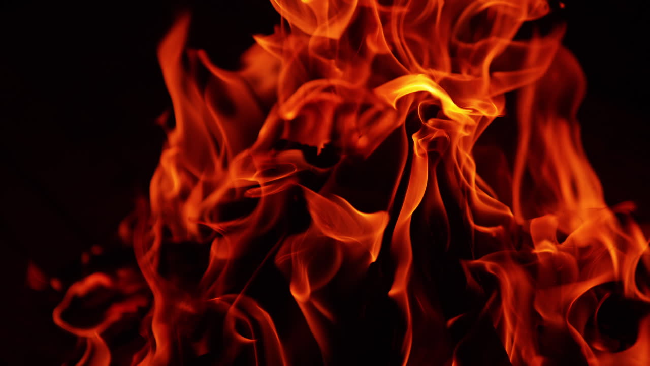 Dark chops of wood in the flames on bonfire. Close up view of the campfire at black backdrop.