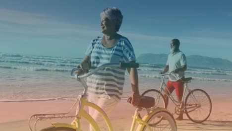 spots of light against african american senior couple with bicycles walking together at the beach