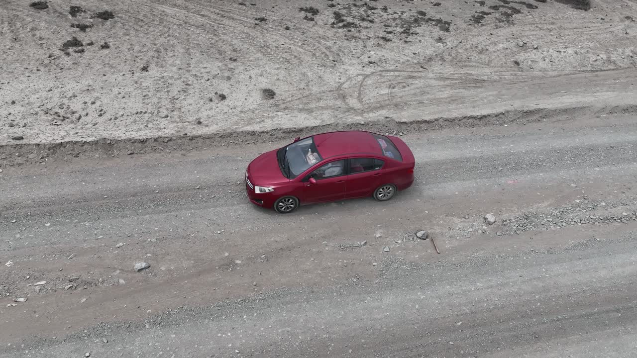 toma panorámica aérea de un coche rojo que conduce a lo largo de una carretera rural seca y polvorienta hacia la ciudad santa de caral con vistas al desierto y las colinas en el fondo