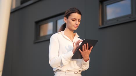 businesswoman walking walking past modern building with a tablet in her hand