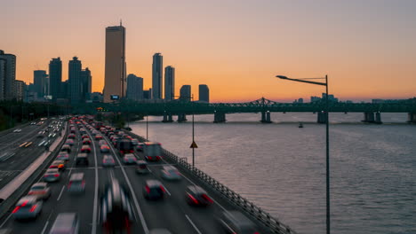 Cars-Moving-in-Seoul-Downtown-District-at-Sunset-on-Olympic-Expressway-and-63-Building-in-Yeouido-nearby-Han-River,-Gangnam-gu-and-Yeongdeungpo-gu,-South-Korea---zoom-out-timelapse