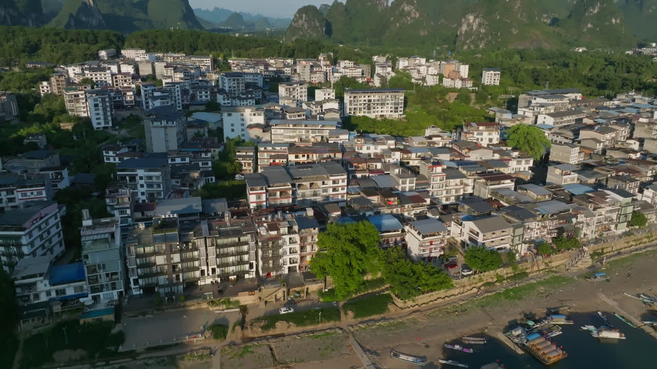 Aerial view descending in front a riverside community in Yangshuo, sunset in China