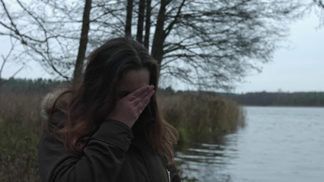 Sad young woman is standing on the bank of the lake