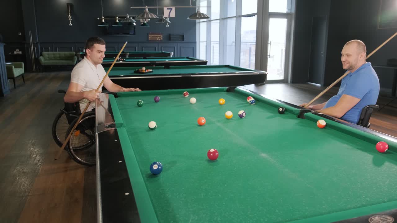 Adult men with disabilities in a wheelchair play billiards in the club