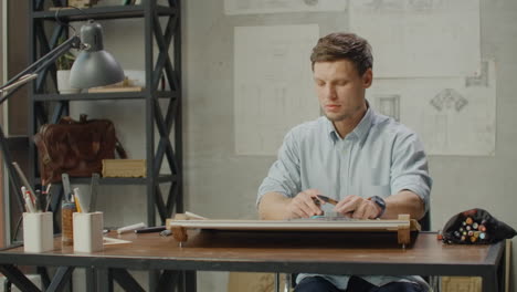 Architect-man-sits-at-drafting-table-in-modern-industrial-office-during-the-day.-Architect-working-on-blueprint-with-spesial-tools-and-pencil-close-up.-Male-architect-at-work-only-hands-with-ruler-and-pencil.-Design-of-the-house.-Engineer.-Tools-for-drawing.-Creating-a-drawing.