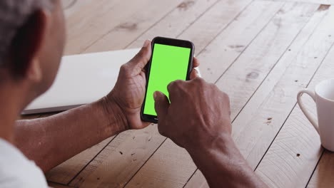 Over-shoulder-view-of-a-senior-black-man-sitting-at-a-wooden-table-using-a-smartphone,-close-up