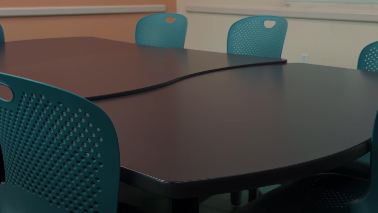 Slow motion upward glide across empty meeting table and blue chairs in modern room