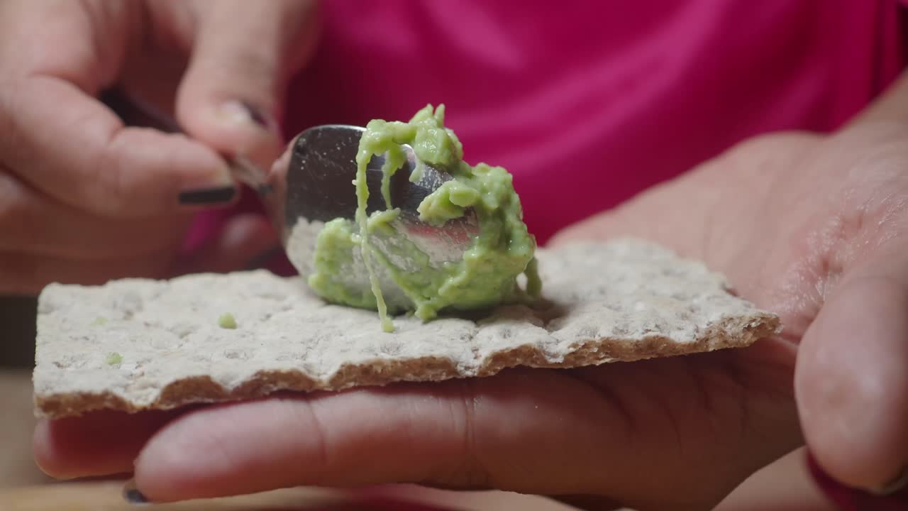 Primo piano di una mano che spalma crema di avocado su pane croccante