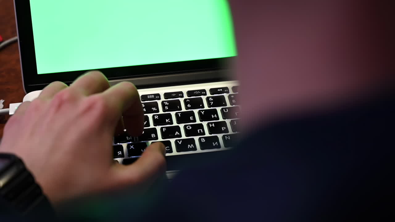 Close up of a man typing on a laptop with a green screen
