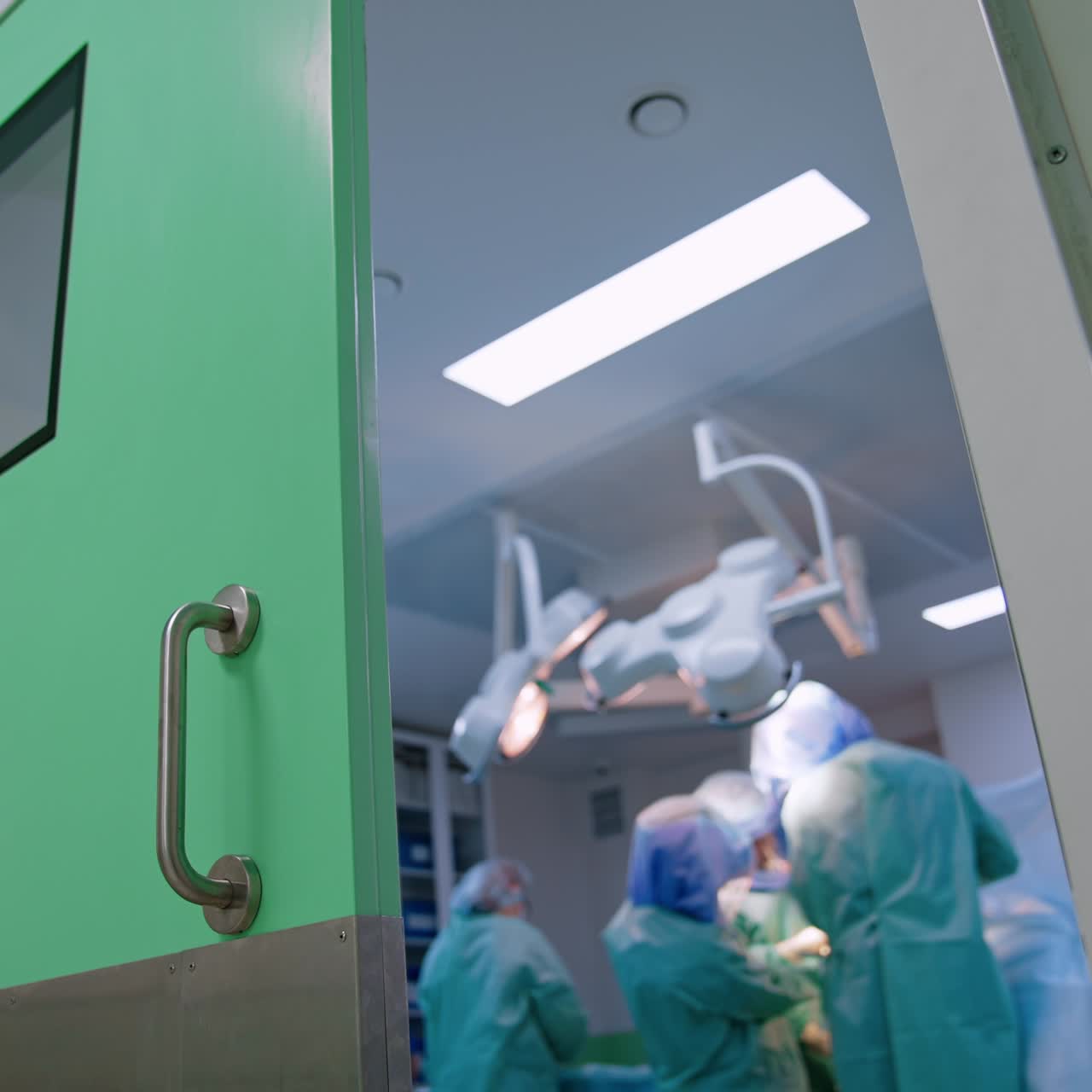 Light blue door half opened to a surgery room. Doctors' team performing operation inside. Low angle perspective