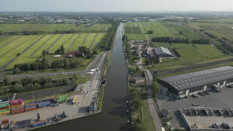 linear aerial movement over a long canal running through green fields and industrial sites, highlighting classic dutch water management and infrastructure