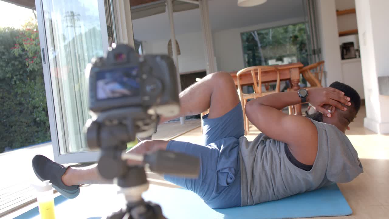 vlogger de fitness masculino afroamericano haciendo ejercicio y filmando en casa, cámara lenta
