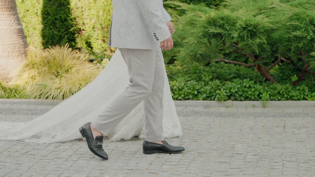Pengantin pria berjalan di depan dengan gaun panjang pengantin wanita menjuntai anggun di belakang