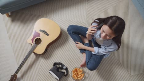 top view of asian teen girl talking on smartphone while sitting on carpet on the floor at home