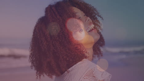 animación de llamaradas de lente sobre el retrato de una joven biracial con cabello afro riendo en la playa.
