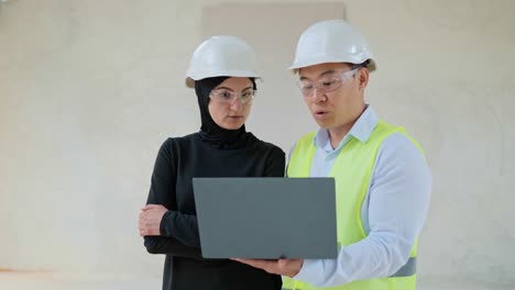 portrait of successful real estate arabian muslim investor and chinese engineer standing indoors in empty building wearing safety helmet and formal suit. international business. buying apartment.