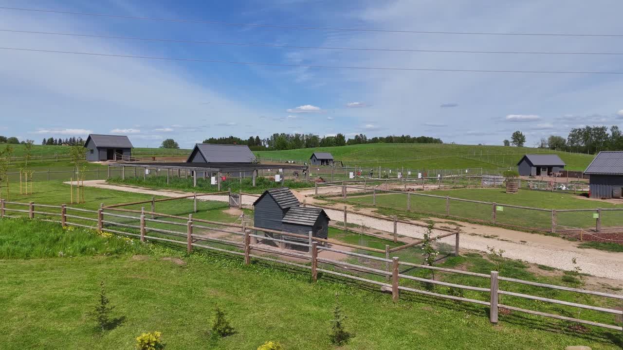 Low-angle drone shot showing fenced pens, wooden barns, and open grassy enclosures at small Zoo, a family-friendly petting farm surrounded by gentle hills and rural countryside