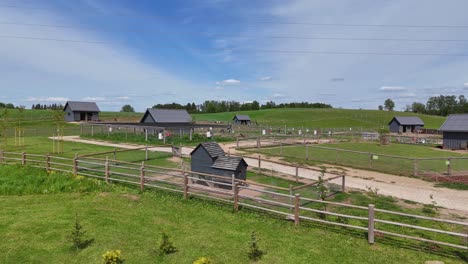 low-angle drone shot showing fenced pens, wooden barns, and open grassy enclosures at small zoo, a family-friendly petting farm surrounded by gentle hills and rural countryside
