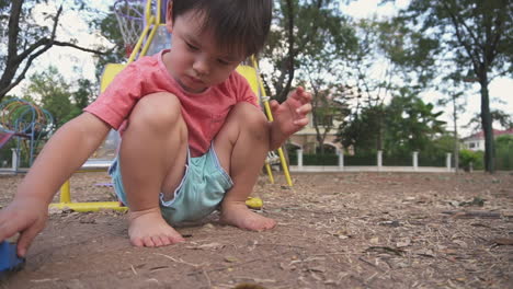 slow motion close up clip of an east asian boy kid having fun playing with a toy truck sitting on the floor of an outdoor park after school