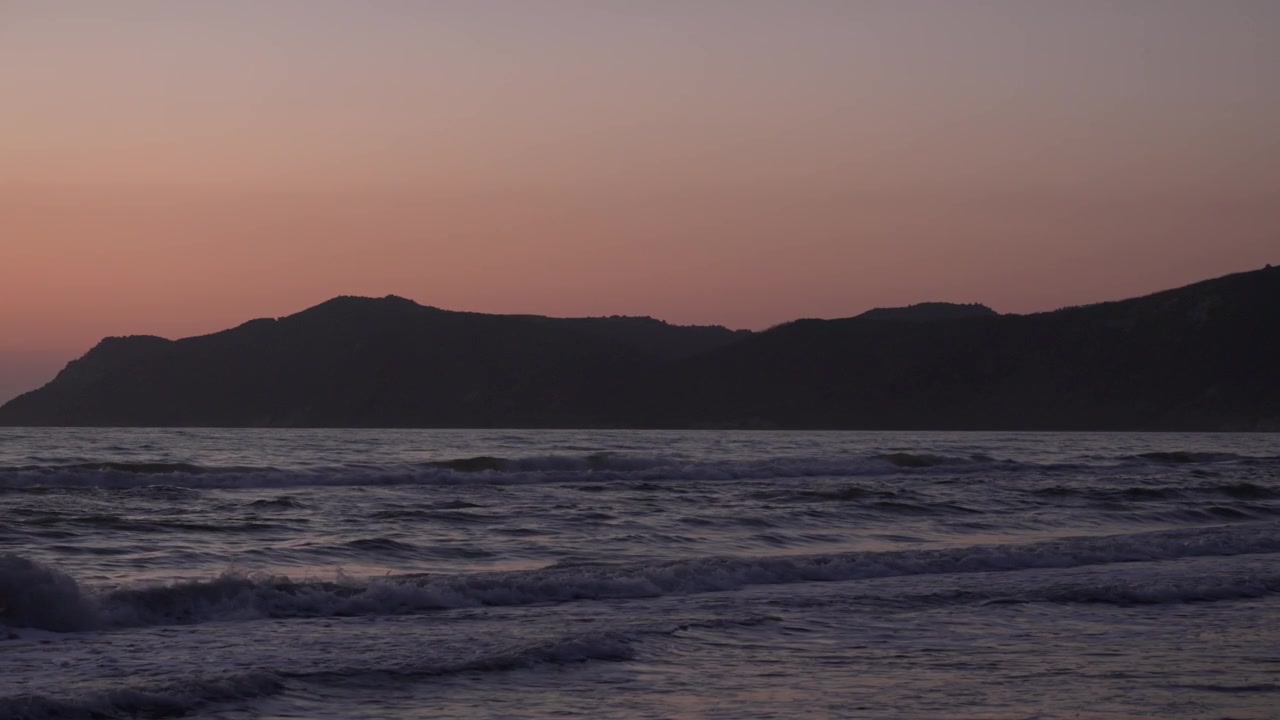 Havbølger i slowmotion med en levende orange skyline ved solnedgang, et roligt og fredfyldt naturøjeblik
