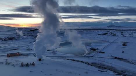 white steam from chimneys of myvatn geothermal plant in snowy icelandic landscape after sunset