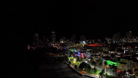 Hermosas-Imágenes-Nocturnas-De-Drones-Aéreos-De-Miami,-EE.-UU.:-Movimiento-Giratorio-Que-Muestra-La-Costa-Con-Palmeras-Y-Muchas-Luces-De-Diferentes-Colores-Sobre-Los-Edificios