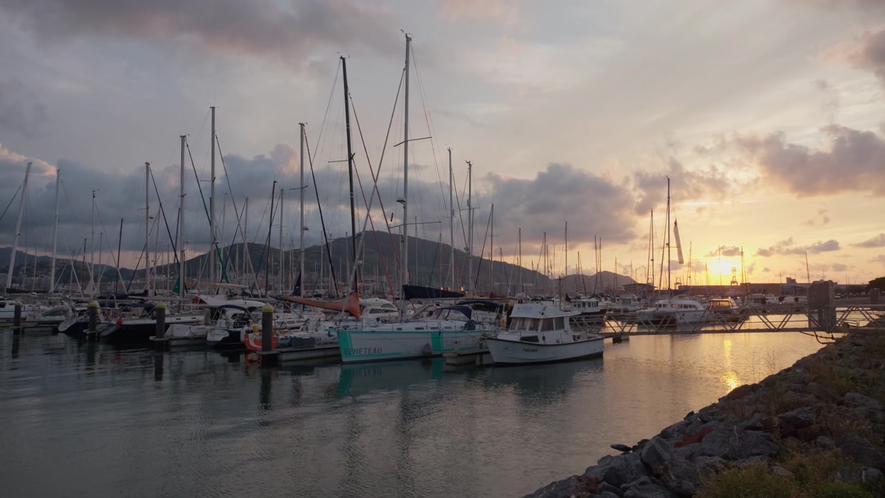 Barche a vela ormeggiate in una tranquilla marina di Algorta al tramonto, che riflettono una luce calda sull'acqua calma, con montagne sullo sfondo