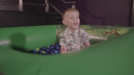 a young boy plays in ball pit and throws balls around whilst smiling - ungraded