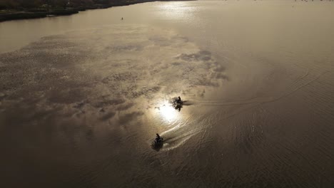 slow motion aerial shot of two motorcycles driving over water surface at sunset after strong rain