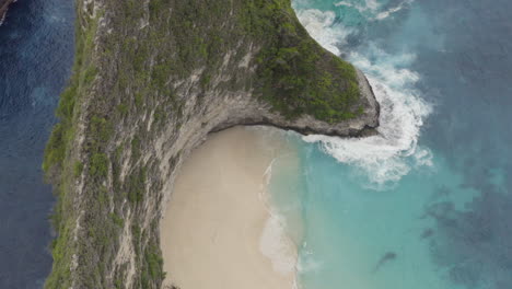 bird eye top view on kelingking beach with tourists down below and the peninsula with a walk path, nusa penida, bali, indonesia. aerial shot.