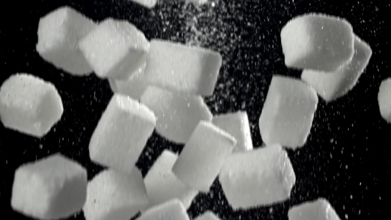 Hvite sukkerbiter faller i sakte film på svart bakgrunn