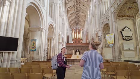 dos visitantes mujeres caminan por el amplio y grandioso interior de la catedral de norwich con asombro.