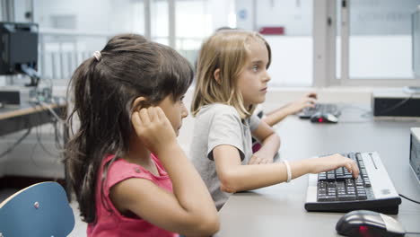 niñas multiétnicas escribiendo juntas en el teclado durante la lección de informática