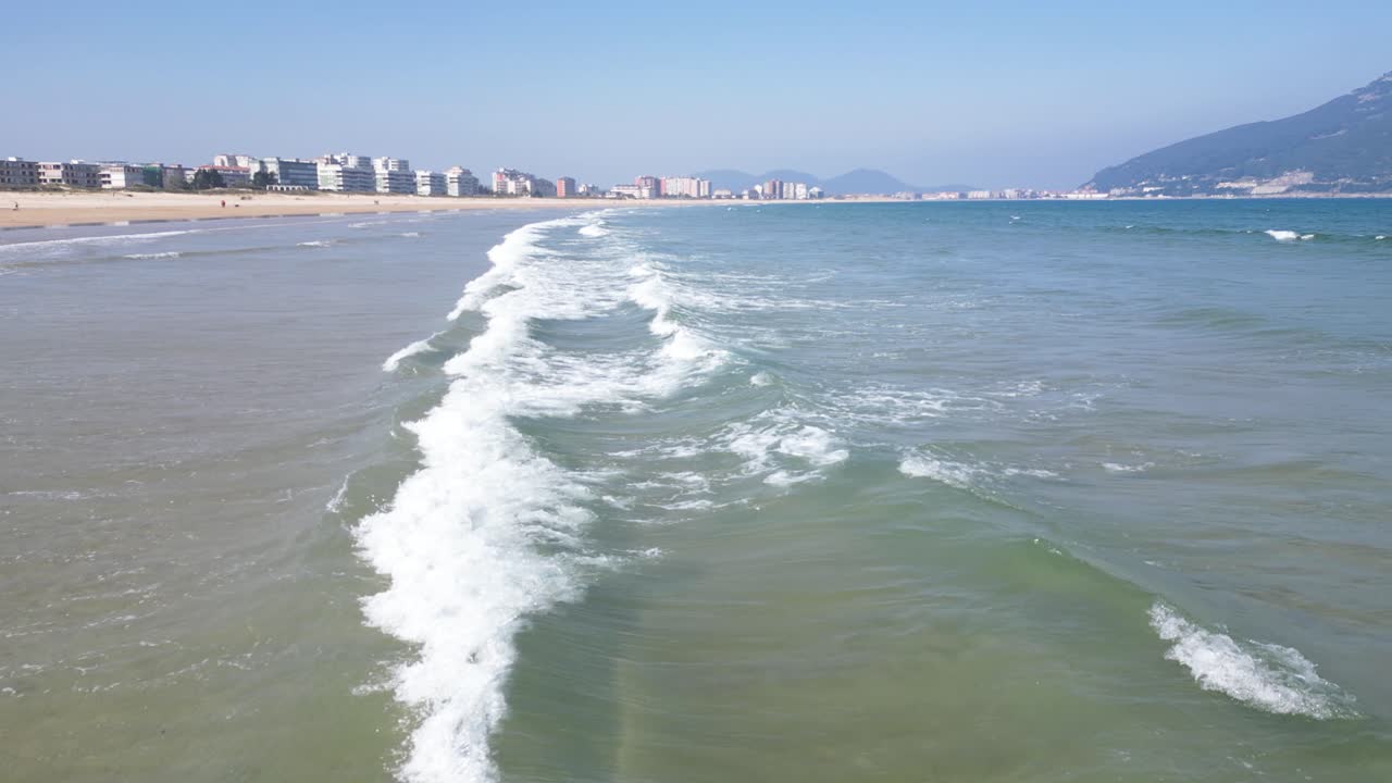 Oceano com ondas espumosas banhando a costa arenosa sob a luz do sol na Cantábria, Espanha.